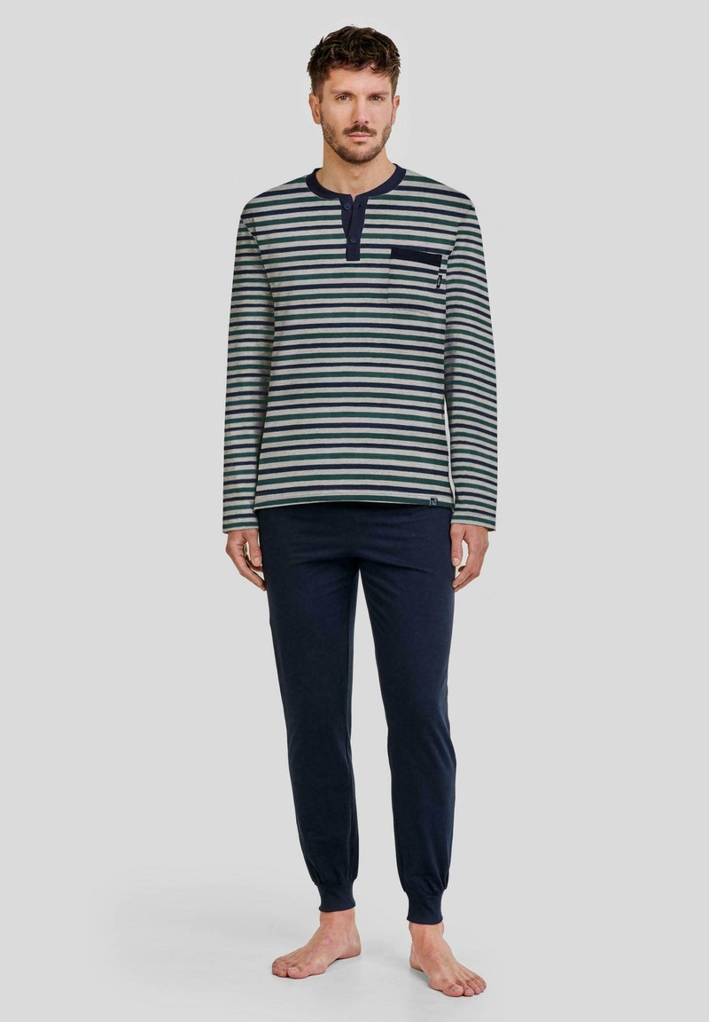 Camisa de manga larga a rayas en verde y crema con un bolsillo en el pecho, combinada con pantalones azul marino sólidos con tobillos ajustados, confeccionados en tejido suave.