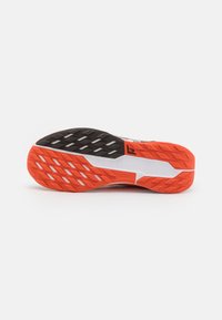 Sål af sko med et tekstureret design i sort og orange gummi, som har et geometrisk mønster for skridfasthed og stabilitet, mærket "All Terrain Compound."