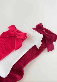 Drei gefaltete Strumpf aus Wolle in Rot, Weiß und Burgund, jeweils verziert mit einer passenden Satin-Schleife nahe dem oberen Saum.