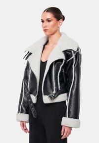 Giubbotto cropped in pelle nera con collare e polsini in shearling bianco, con hardware in metallo e dettagli con tasche con zip.