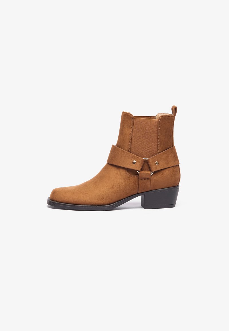 Brown suede ankle boot with a flat heel, featuring an elastic side panel and a wide strap across the midfoot with a round hardware accent.
