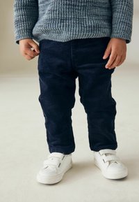 Outfit per bambino composto da un maglione di maglia blu testurizzata e pantaloni di velluto a coste blu scuro, abbinati a sneaker bianche con chiusura a velcro.