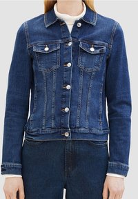 Tmavě modrá džínová bunda s přiléhavým střihem. Obsahuje dvě náprsní kapsy, stříbrné knoflíkové zapínání a detaily s kontrastním šitím.