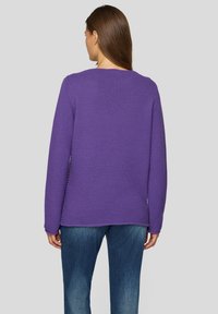 Lila Strickpullover mit strukturierter Oberfläche, weiten Ärmeln und rundem Halsausschnitt, kombiniert mit blauen Jeans.