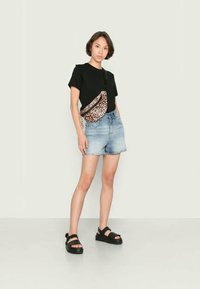 T-shirt preto, calções de ganga rasgados e sandálias de plataforma pretas. Uma bolsa cruzada de estampado de leopardo adiciona um detalhe contrastante ao conjunto.