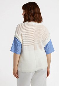 Biały sweter robiony na drutach z otwartym splotem i krótkimi, niebieskimi, paskowanymi rękawami. Charakteryzuje się luźnym krojem, ściągaczem u dołu i fakturowanymi wzorami.