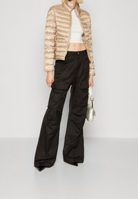 Beige Steppjacke mit gestepptem Muster, kombiniert mit schwarzen Cargo-Hosen mit mehreren Taschen und weitem Bein. Silberne Handtasche.