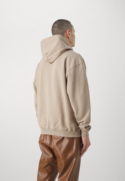 Sudadera beige con capucha de corte relajado, textura suave, puños y dobladillo acanalados, combinada con pantalones de piel sintética marrón brillante.