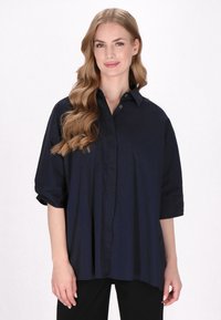 Marineblaue Oversized-Shirt mit durchgehender Knopfleiste, kurzen Ärmeln und glattem Stoff, das eine entspannte Passform und einen abgerundeten Saum aufweist.