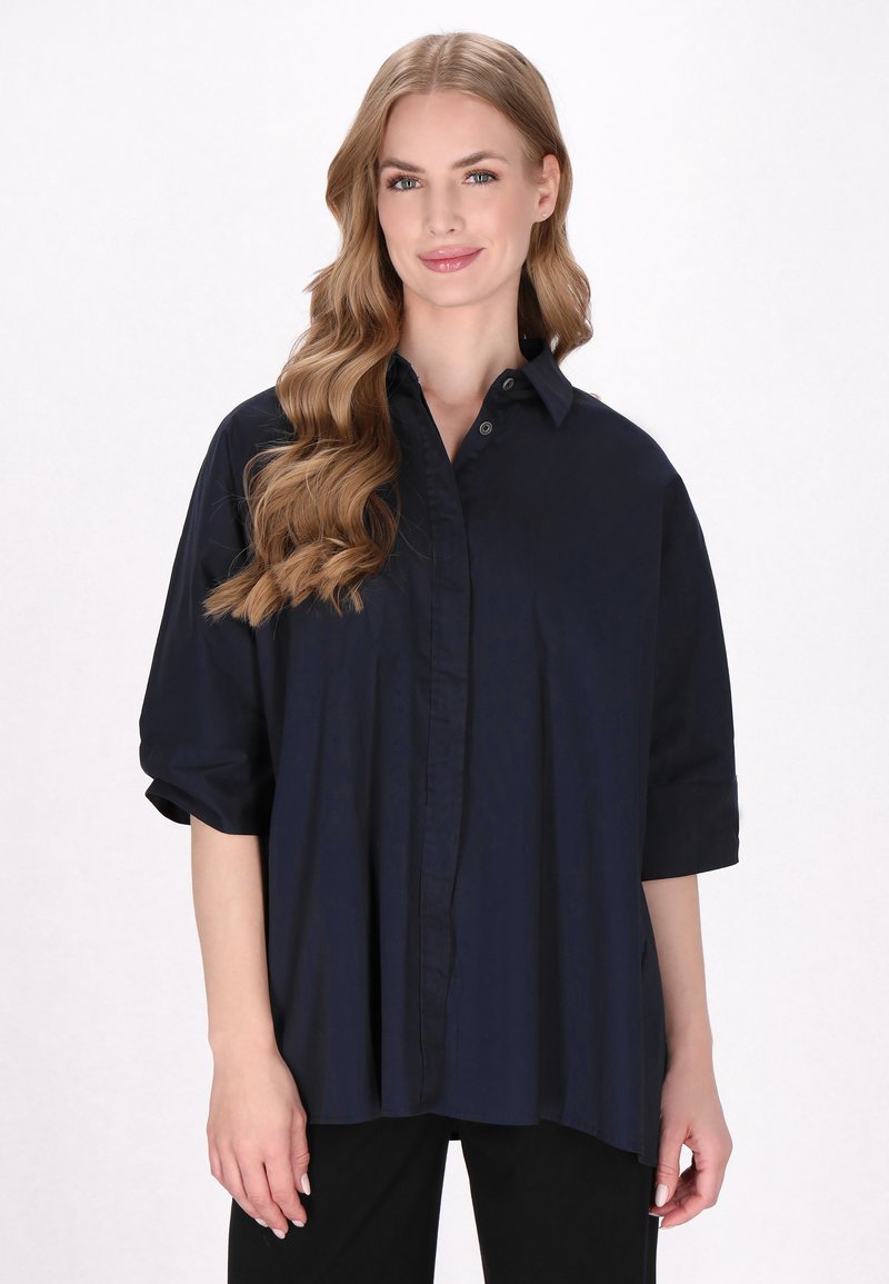 Marineblaue Oversized-Shirt mit durchgehender Knopfleiste, kurzen Ärmeln und glattem Stoff, das eine entspannte Passform und einen abgerundeten Saum aufweist.