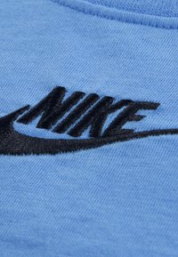 Φούτερ με επωνυμία Nike σε ανοιχτό γαλάζιο βαμβάκι· διαθέτει μαύρο κεντημένο λογότυπο με σχέδιο swoosh στο μπροστινό μέρος. Διακριτή υφ ή υφάσματος ορατή.