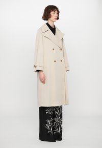 Beige double-breasted trench coat with large lapels, gold-tone buttons, and wide sleeves. Features a loose fit and soft texture.