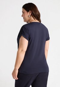 Tricou navy cu mânecă scurtă și manșete rulate, textură netedă, guler rotund și o croială lejeră, asortat cu pantaloni închiși la culoare.