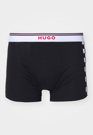 Juodi bokseriai su balta juosta, ant kurios raudonai užrašyta "HUGO". Šone yra languotas raštas su kontrastingais baltais ir juodais kvadratais.