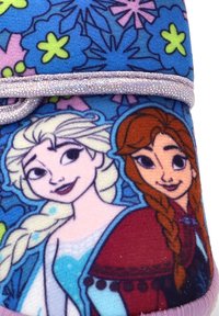 Dos personajes animados femeninos con cabello trenzado, uno vestido de blanco y azul, y el otro de rojo, rodeados de patrones florales en azul y púrpura.