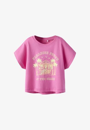 Camiseta rosa de manga corta con una casa de playa, palmeras, pájaros y el texto "Paraíso Encontrado en la Playa" impreso en amarillo claro.