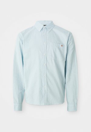 Light blue long-sleeve button-up shirt with buttoned collar and chest pocket featuring a small red and white logo patch.