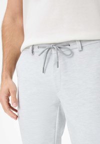 Light gray jogger pants made of textured fabric, featuring a drawstring waist with gray accents. The design includes slanted side pockets.