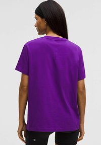 Violeta kokvilnas T-kreklu ar īsām piedurknēm, brīvs piegriezums un taisna apakša. Uz apakšējās apmalītes atrodas neliels logo.