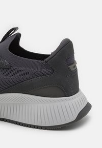 Szary but sportowy z teksturowaną siateczkową cholewką, zamszowymi akcentami, grubą gumową podeszwą oraz pętelką na pięcie ułatwiającą zakładanie.