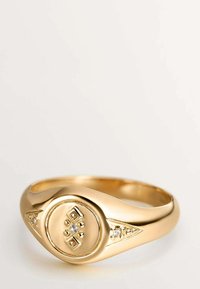 Anillo de oro con una banda lisa y redondeada que presenta un frente circular con acentos similares a diamantes y diseños geométricos grabados.