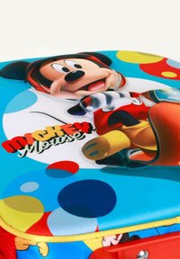 Mochila azul con una tela brillante que presenta a Mickey Mouse, puntos de colores y un acento rojo, asegurada con una cremallera amarilla y un asa roja.