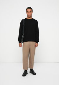 Sweater de malha preto, calças largas bejes e mocassins pretos. A modelo leva uma mala preta de ombro com alça e ferragens metálicas.