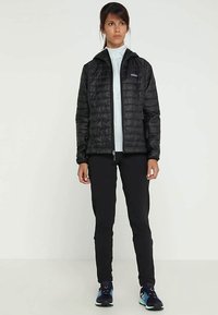 Čierna izolovaná bunda so zipsom vpredu, kapucňou, prešívaným vzorom, v kombinácii s čiernymi nohavicami a modrými športovými topánkami.