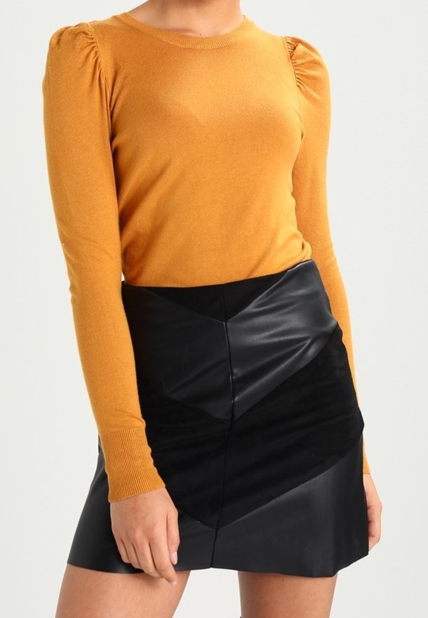 Senapsgul långärmad topp med skräddarsydda axlar, tillsammans med en svart faux läder minikjol med ett geometriskt mönster.