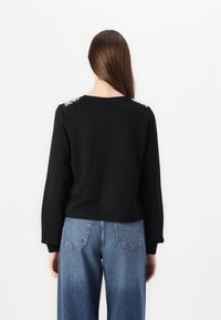 Μαύρη φούτερ μπλούζα με μακριά μανίκια και στενή εφαρμογή. Διαθέτει διακοσμητικά στοιχεία στους ώμους. Συνδυάζεται με τζιν παντελόνι ψηλής μέσης.