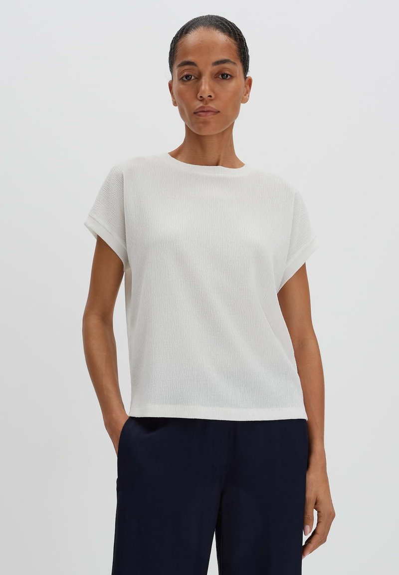 Top bianco dalla vestibilità morbida con maniche corte arrotolate, realizzato in tessuto testurizzato. Semplice scollatura rotonda, abbinato a pantaloni blu scuro.