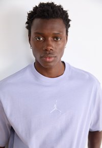 Lyse lilla bomulds T-shirt med et hvidt Jumpman-logo på brystet. Rund halsudskæring og korte ærmer med en glat tekstur.