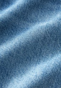 Denimska tkanina, srednje teže, svetlo modre barve z rahlo teksturo. Ima diagonalno tkane vlaknine in rahlo bledenje na nekaterih mestih.