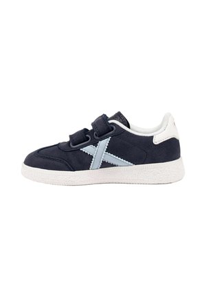 Zapatilla deportiva azul oscuro con detalle de cruz azul claro, lengüeta trasera blanca, suela blanca y dos tiras de velcro ajustables sobre fondo blanco.