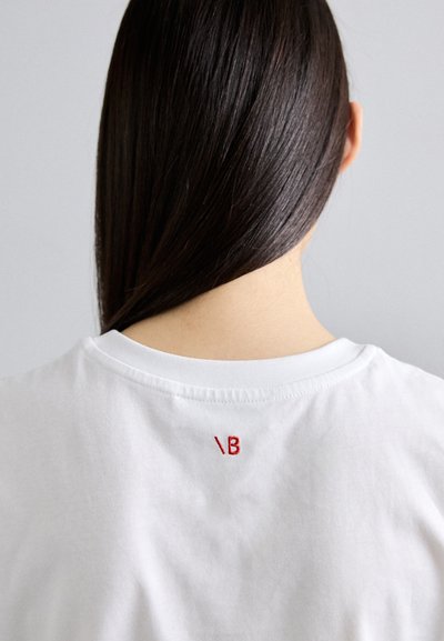 Weißes Baumwoll-T-Shirt mit rundem Ausschnitt. Verfügt über roten gestickten Text „\B“ auf dem Rücken, glatte Textur und lässige Passform.