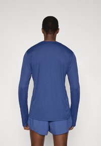 Αθλητική μπλούζα μακρυμάνικη σε ναυτικό μπλε χρώμα από λείο, ελαφρύ ύφασμα. Διαθέτει στρογγυλή λαιμόκοψη και άνετη εφαρμογή.