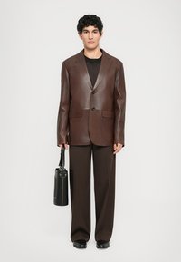 Brown leather blazer with notched lapels, two buttons, and two front pockets, paired with dark brown wide-leg trousers and a black bag.