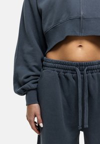 Felpa cropped grigio scuro con collo zip e maniche voluminose, abbinata a pantaloni della tuta con coulisse elasticizzati.