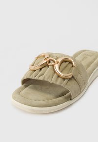 Sandal cu toc din suede verde, cu un brâu căptușit, având un accent cu hardware circular de nuanță aurie și o talpă texturată.