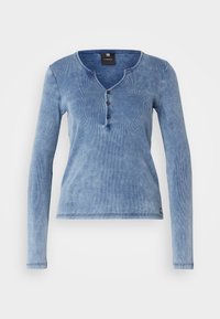 Långärmad, ljusblå ribbad topp med henley-krage, tre knappar och en texturerad yta. Mjuk tyg med subtila färgvariationer.