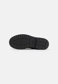 Suela de zapato de goma negra con una banda de rodadura estampada, que presenta un acento rectangular etiquetado "BOSS" en el centro. Superficie texturizada para mejorar el agarre.
