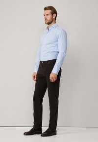 Lichtblauw overhemd met lange mouwen, zwarte broek en donkere schoenen. Het overhemd heeft een slim fit ontwerp, lange mouwen en subtiele knoopaccenten.