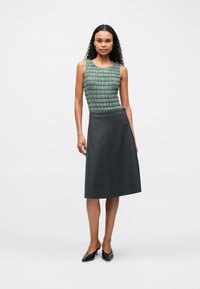 Šviesiai žalia tekstūruota be rankovių palaidinė su apvalia iškirpte ir tamsiai pilku klostuotu sijonu, derinama su juodais smailiais bateliais.