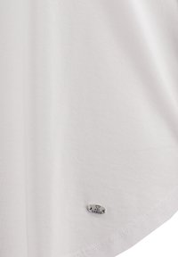 Weißes Kurzarmoberteil aus glattem, leichtem Stoff. Hat einen abgerundeten Saum und ein kleines Metall-Logo.