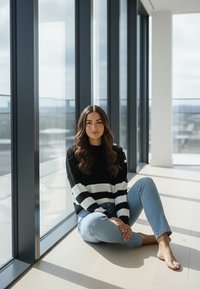 Czarno-biały sweter w paski z okrągłym dekoltem, zestawiony z jasnoniebieskimi dżinsami, siedzący na jasnej drewnianej podłodze obok dużych okien.