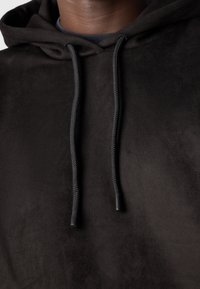 Gros plan d'une personne portant un sweat à capuche noir avec des cordons tressés visibles et une texture de tissu lisse.