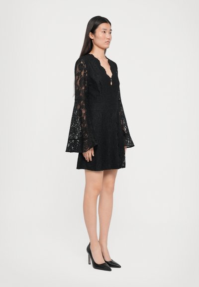 Black lace dress featuring long sheer bell sleeves, a scalloped V-neckline, and a fitted waist, paired with black high-heeled shoes.