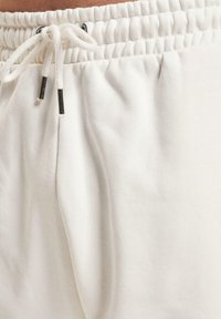Lys beige sweatpants med elastisk talje, snor lukning og blød bomuldsstruktur; skjulte sidelommer er synlige.