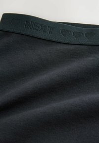 Tessuto nero con una consistenza liscia, caratterizzato da una cintura elastica verde scuro con il marchio "NEXT" e motivi a forma di cuore.