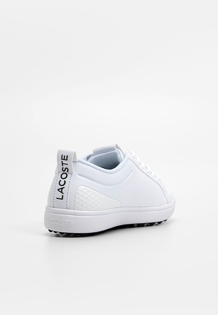 Zapatilla deportiva blanca con un upper sintético suave, acentos texturizados en el lateral y una suela de goma con pequeñas protuberancias para agarre. Marca "LACOSTE" en el talón.